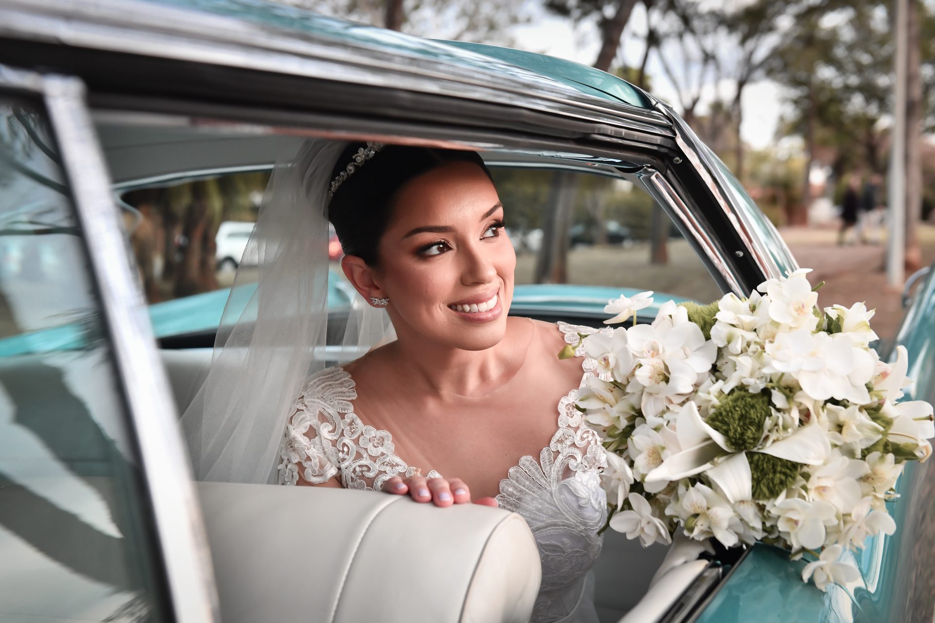 Noiva sorrindo com o buquê dentro de carro clássico azul
